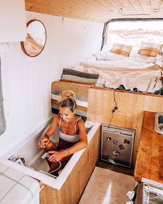 a woman sitting in a sink inside of a small room next to a stove top oven