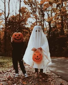 two children dressed up as ghost and pumpkins walking down the road with their hands in each other's pockets