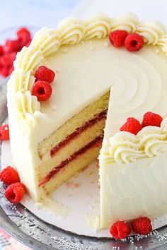 a cake with white frosting and raspberries is cut in half on a plate