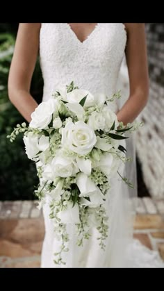 a bride holding a bouquet of white flowers in her wedding dress and standing on a stone walkway