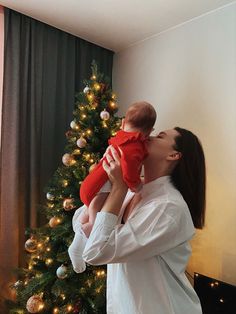 a woman holding a baby in front of a christmas tree