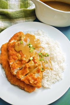 two pieces of fried chicken covered in gravy on top of rice and sauce