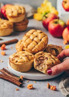 a person picking up an apple pie from a plate with cinnamon sticks and apples in the background