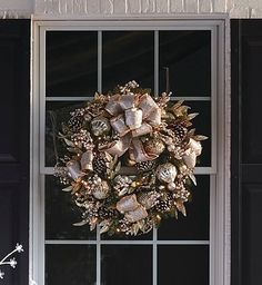 a wreath on the window sill with pine cones and other holiday decorations hanging from it