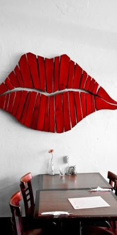 a wooden table topped with red chairs next to a wall mounted art piece on the wall