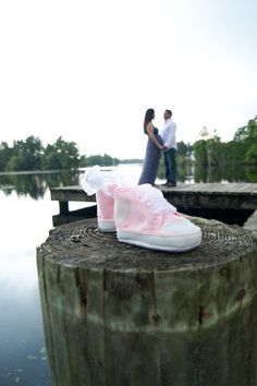 a pair of shoes sitting on top of a wooden post next to the water in front of a man and woman