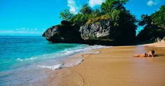 a woman laying on top of a sandy beach next to the ocean