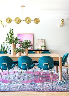 a dining room table with blue chairs and potted plants on the rug in front of it