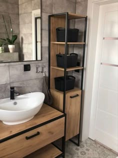 a bathroom sink sitting under a mirror next to a wooden shelf filled with black baskets