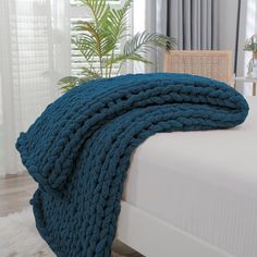 a blue blanket on top of a bed next to a chair and potted plant