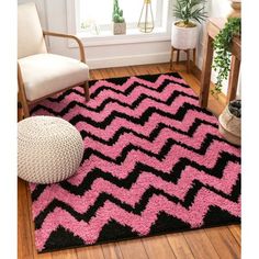 a black and pink area rug on a wooden floor next to a chair with a plant in the corner