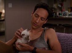 a man holding a small white cat in his lap while sitting on a couch next to a bar