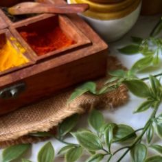 a wooden box filled with lots of different colored powders next to some green leaves