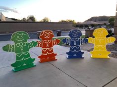 three wooden gingerbread men standing in front of a house on the sidewalk with their arms around each other