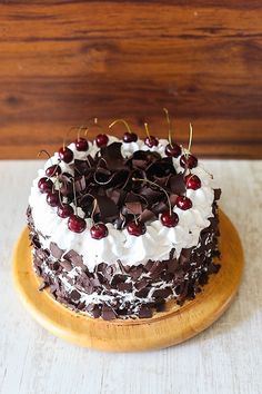 a chocolate cake with white frosting and cherries sitting on top of a wooden plate