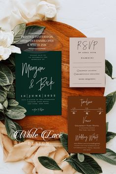 the wedding stationery is laid out on top of a wooden platter with flowers and greenery