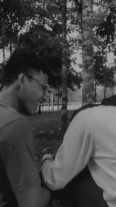 black and white photograph of two men sitting on a bench in the park with trees