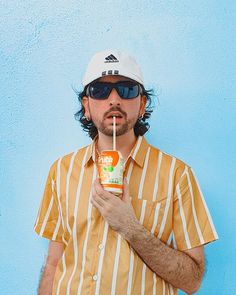 a man in sunglasses and a hat holding a drink with a straw sticking out of it