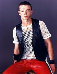 a man sitting on top of a stool wearing red pants and a black vest over his shirt