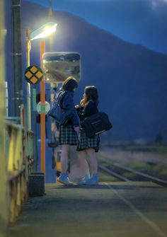 two girls are standing on the train tracks at night with their backs to each other