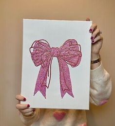 a woman is holding up a pink bow on a white canvas with sequins