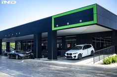 two cars parked in front of a building with green trim on the roof and side windows