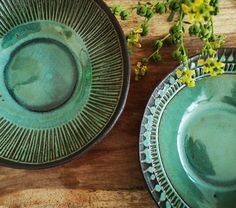 two green plates sitting on top of a wooden table next to yellow and white flowers