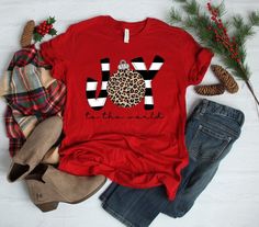 a red shirt with the word joy on it next to some jeans and pine cones