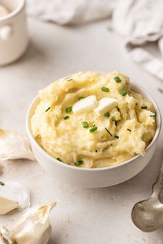 a bowl filled with mashed potatoes on top of a white table next to garlic