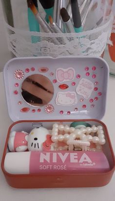 a pink and white tin with hello kitty items in it on a table next to pens and scissors