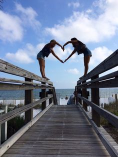 two girls are standing on a wooden bridge with their hands in the shape of a heart