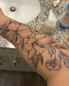 a woman's arm with flowers on it in front of a sink and mirror