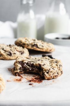 chocolate chip cookies and milk on a white surface with one broken cookie in the foreground