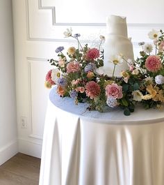 a white wedding cake on top of a round table with flowers around the base and bottom