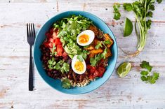 a blue bowl filled with rice, beans and eggs on top of a wooden table