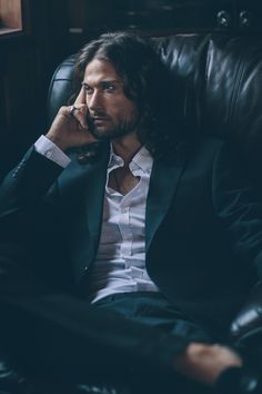 a man sitting in a leather chair talking on a cell phone while wearing a suit and tie