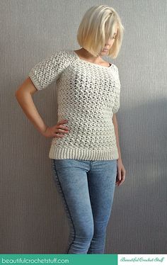 a woman is standing in front of a wall wearing jeans and a knitted sweater