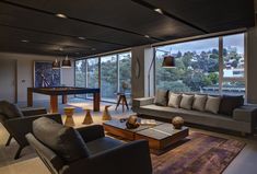 a living room with couches, chairs and a pool table in front of large windows