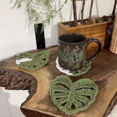 two crocheted coasters and a coffee cup on a wooden table next to a plant