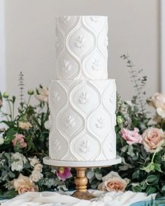 a white wedding cake sitting on top of a table next to flowers and greenery