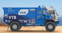 a blue dump truck parked on top of a sandy beach next to the ocean with stickers all over it