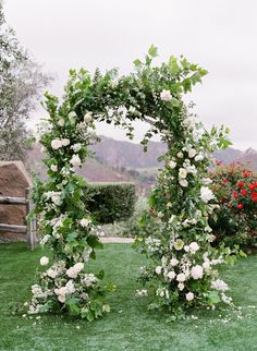 an outdoor wedding ceremony with white flowers and greenery on the grass in front of mountains