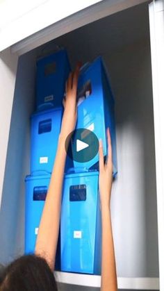 a woman reaching for some blue boxes in a closet with her hands on the shelves