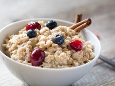 a white bowl filled with oatmeal topped with cherries and cinnamon sticks