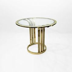 a round glass table with metal legs and a gold frame around the top, against a white background