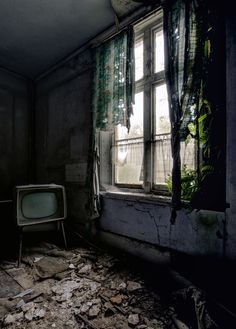 an old tv sitting next to a window in a run down room with debris on the floor