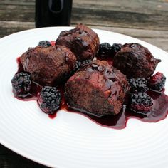 a white plate topped with meatballs covered in blackberry sauce and blackberries next to a bottle of wine