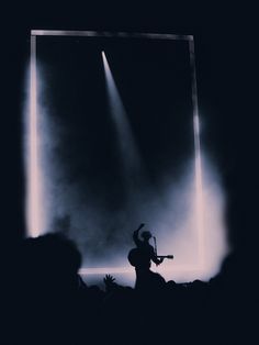 the silhouette of a person holding a guitar in front of a stage with spotlights