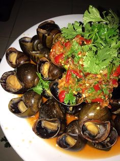 a white plate topped with clams covered in sauce and garnished with parsley