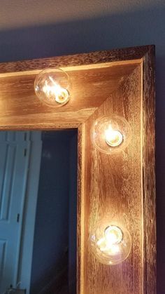 a wooden frame with three lights on the top and one light on the bottom, in front of a mirror